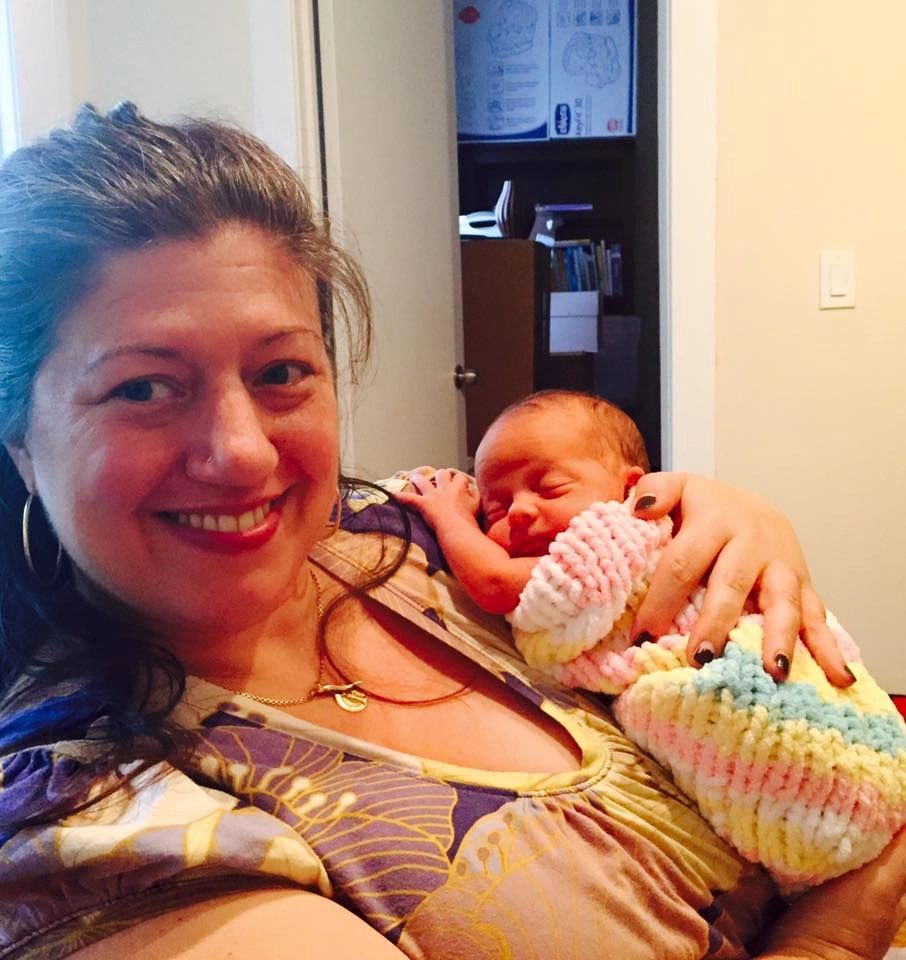 Rita DiRito holding a sleeping newborn wrapped in a knitted blanket